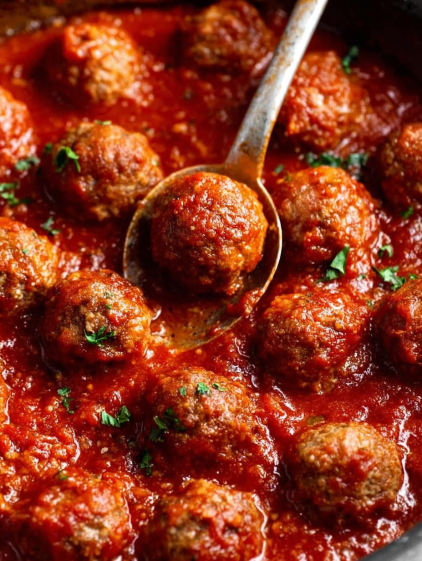 A spoon in a bowl of meatballs.