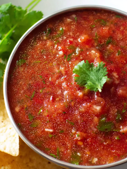 A bowl of red sauce with a green garnish.
