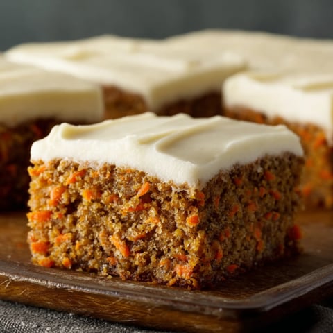 A slice of carrot cake on a wooden cutting board.